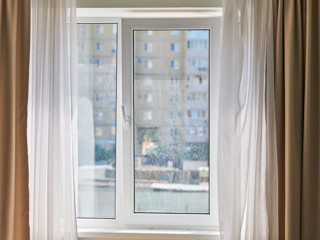 Sunlit window with beige curtains and city view.