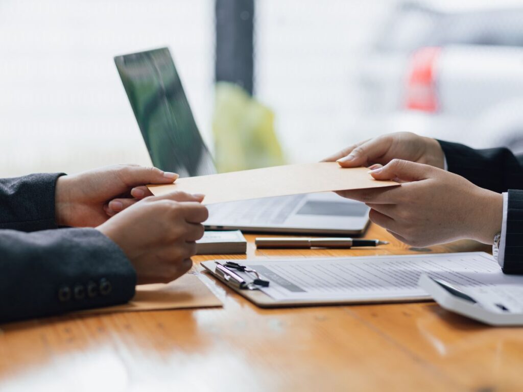 Two people exchanging an envelope at a desk.