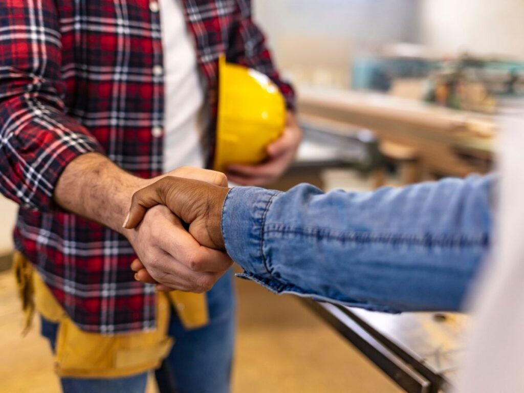 A man holding a yellow hardhat shaking hands with the other person.