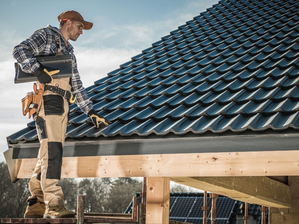 Worker inspecting a roof with blue tiles and wooden structure.