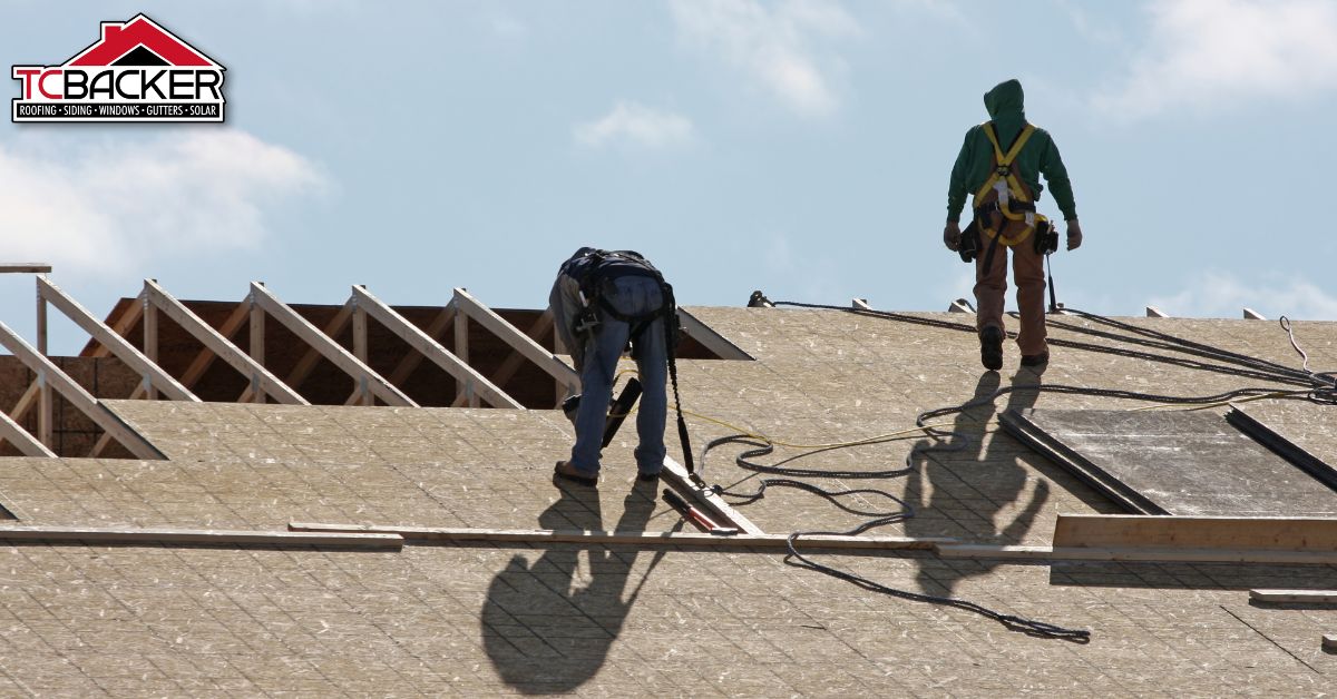 Two workers installing roof decking with safety harnesses on a partially framed roof.