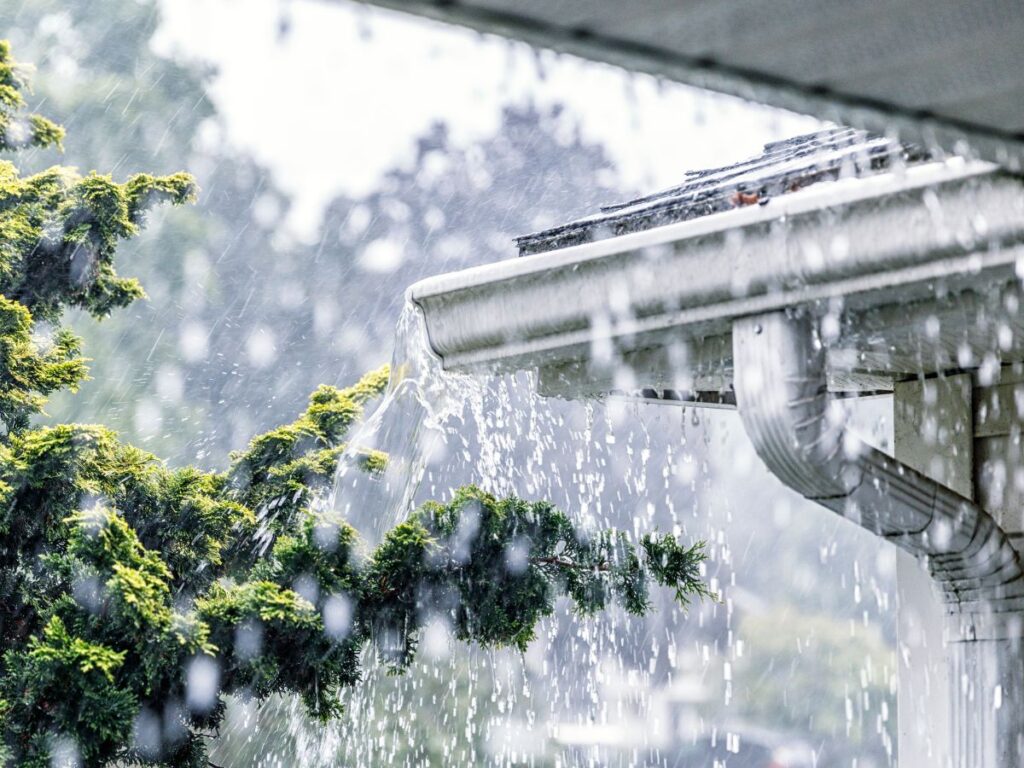 Heavy rainfall overflowing from a clogged gutter.