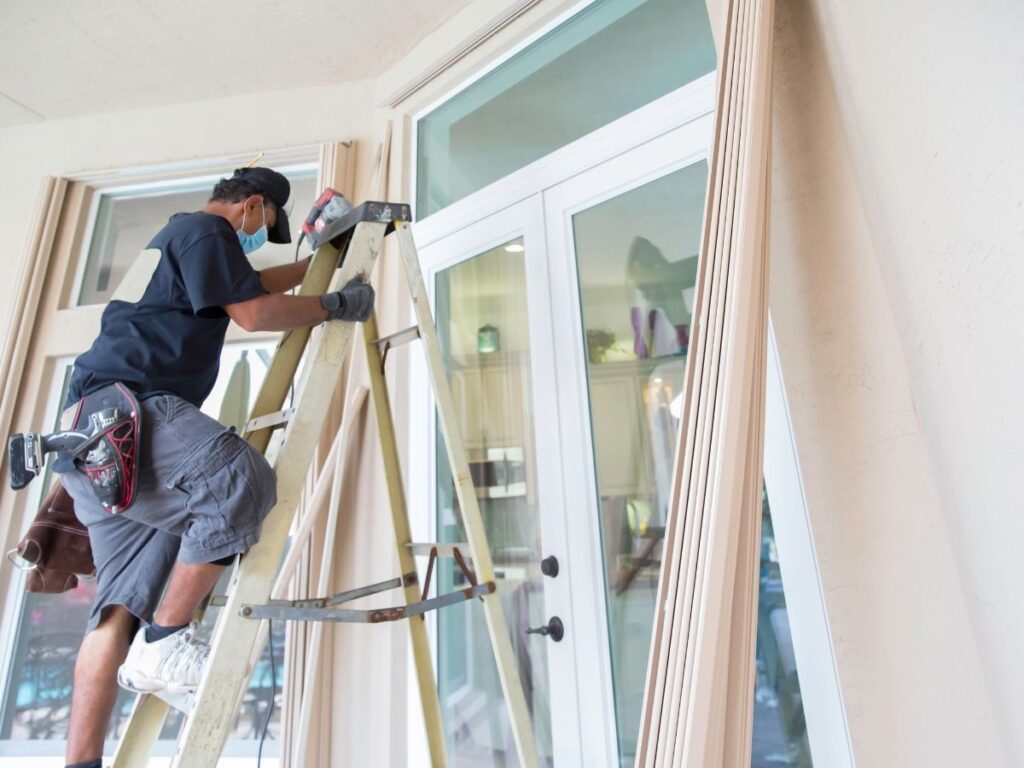 A reapair man going down on the ladder infornt of the glass window.