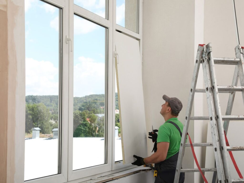 Worker installing a large window pane in a room.