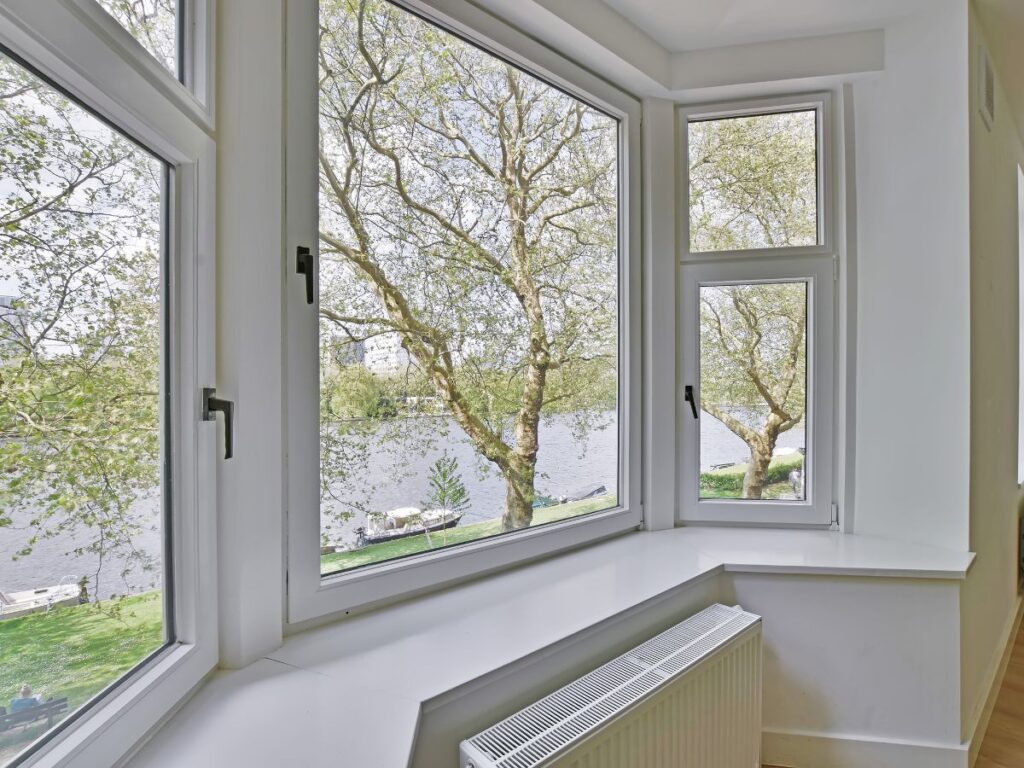 Bay window view of a riverside with trees.