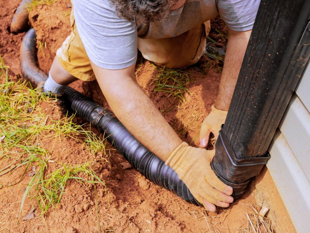 Worker installing a downspout drainage system into the ground.