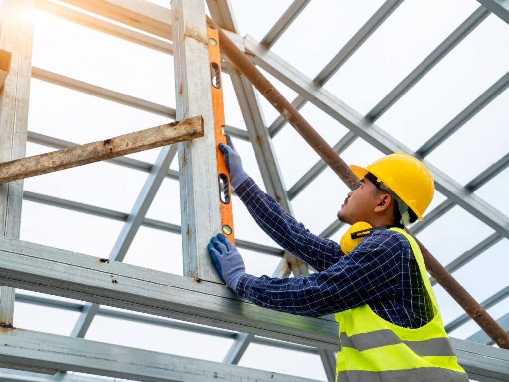 Worker using a level to align metal beams in construction.