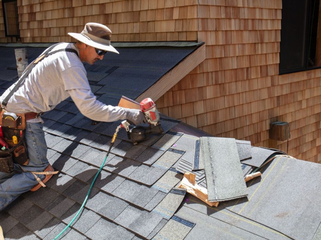 Worker installing shingles using a nail gun on a roof.