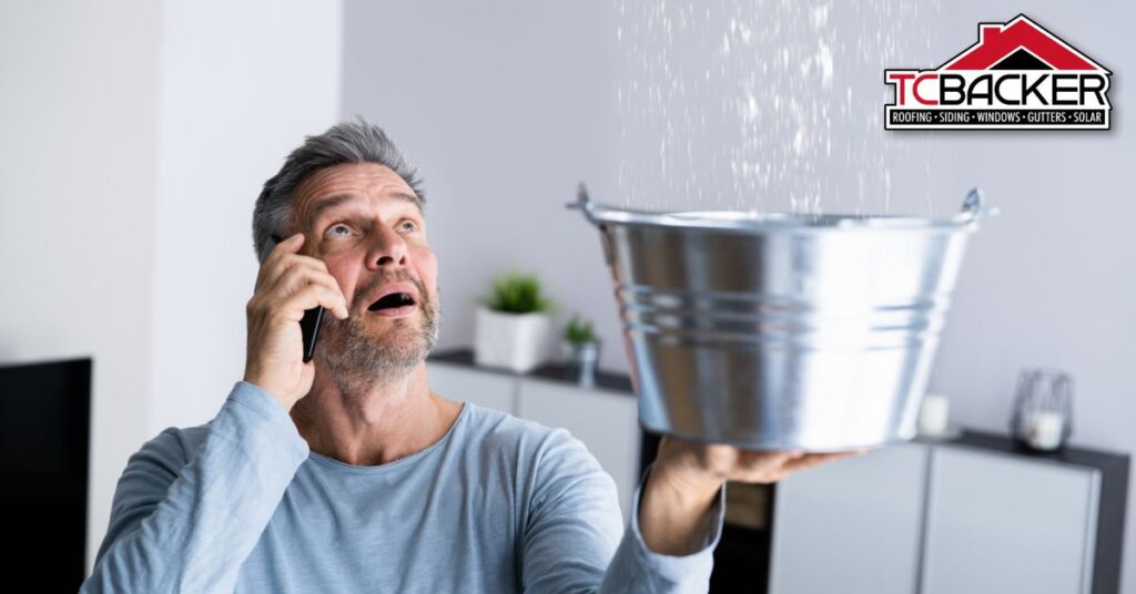 Man catching roof leak in a bucket, talking on the phone.