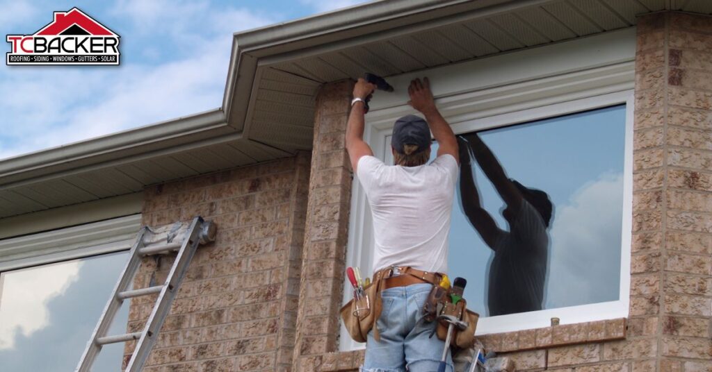 A man on the ladder drilling the siding of a house.