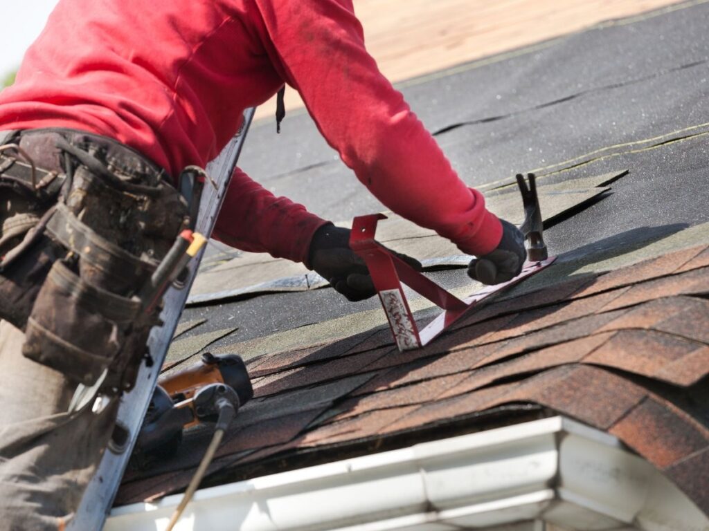 A repair man repairing the roof and hammering it.