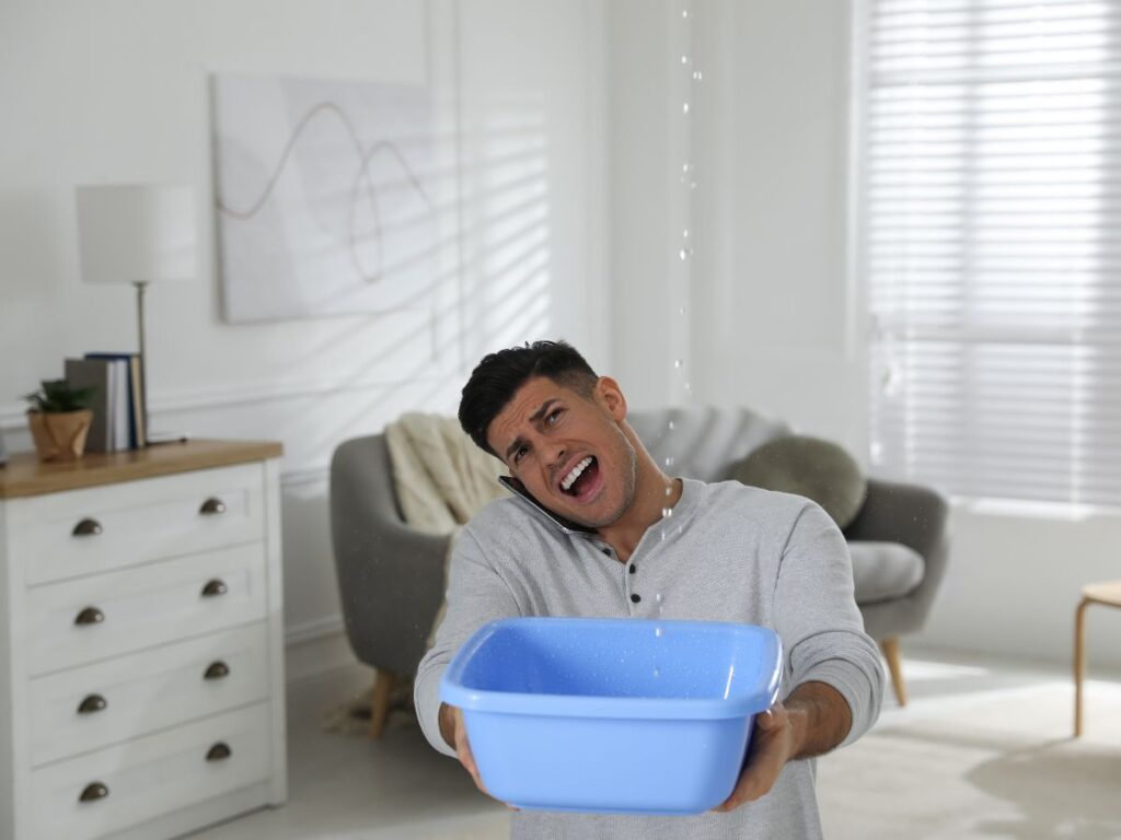 Man catching water in a bucket from a ceiling leak.